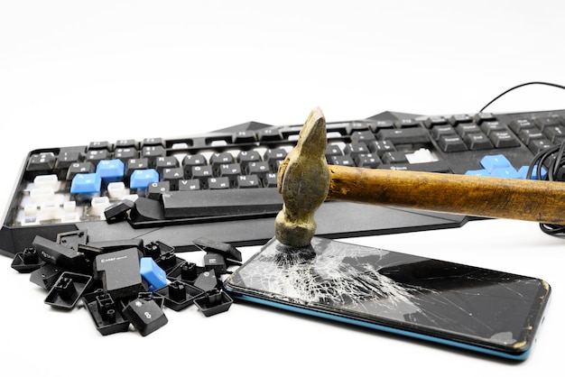 Un clavier cassé et un smartphone cassé brisé avec un marteau de fer se trouvent sur un fond blanc