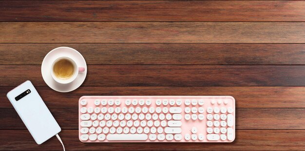 Le clavier de l'ordinateur est de couleur rose et le smartphone sur un fond en bois