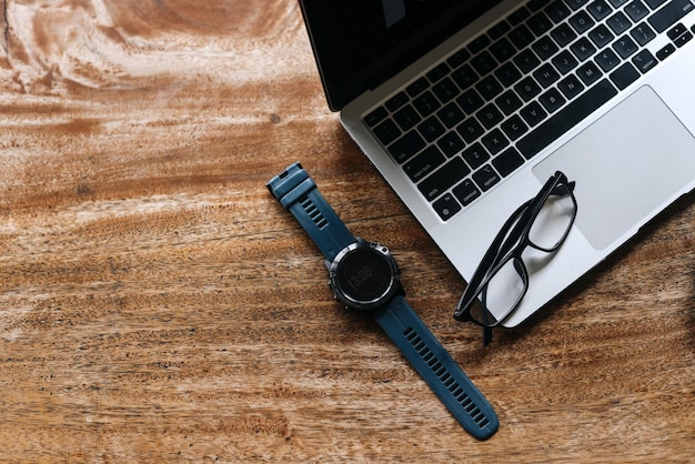 Clavier d'ordinateur portable, montre et lunettes sur la composition de fond en bois. Photo à plat et vue de dessus.