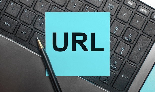 Le clavier de l'ordinateur a un stylo et un autocollant bleu avec le texte URL Uniform Resource Locator Flat lay