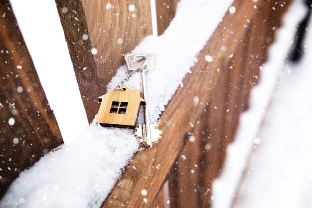 Clé de la maison sur une clôture en bois en hiver dans la neige. Un cadeau pour le nouvel an, Noël. Construire, concevoir, projeter, déménager dans une nouvelle maison, hypothéquer, louer et acheter un bien immobilier. Espace de copie