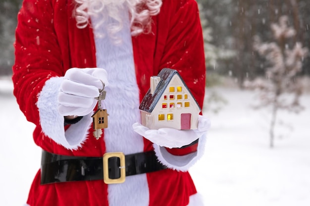 Clé de maison avec porte-clés chalet dans les mains du Père Noël en plein air dans la neige Deal pour l'achat immobilier construction déménagement hypothèque Maison confortable Joyeux Noël nouvel an réservation événement et salle