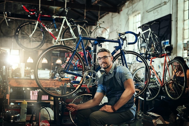 Clé de portrait et mécanicien dans un magasin de vélos ou un atelier de réparation de vélos Technicien de vélo de visage et homme propriétaire d'entreprise sérieux ou professionnel mature avec lunettes et confiance