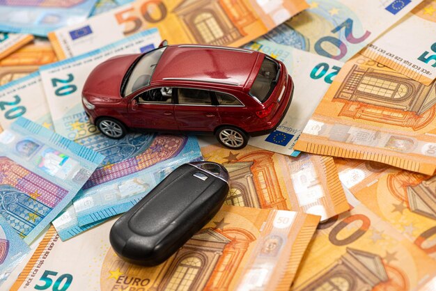 Photo clé et voiture de jouet rouge sur un tas de billets en euros acheter ou vendre une voiture louer une voiture ou concept d'assurance