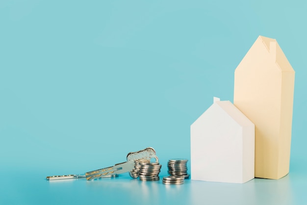 Les clés de la maison; pile de pièces près des maisons de papier sur fond bleu