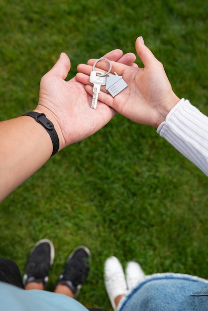 Clés avec un porte-clés sous la forme d'une maison en métal d'une nouvelle maison ou d'un appartement entre les mains d'une jeune famille Le bonheur d'acheter une maison Photo verticale