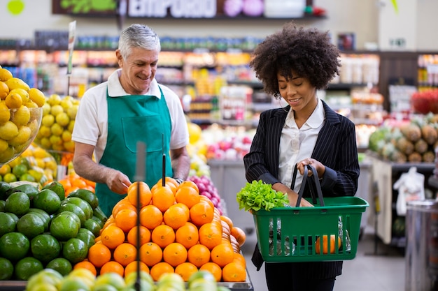 Client africain avec marchand de légumes, tenant des fruits orange.