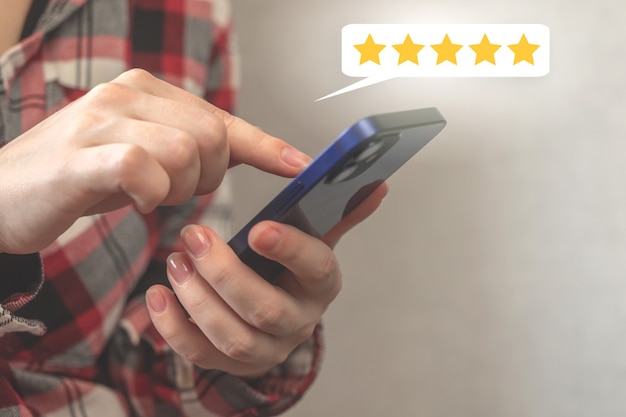 Client appuyant sur l'écran du smartphone avec une note d'or cinq étoiles ou une icône de commentaires, un excellent classement ou le meilleur score pour le service, une photo d'arrière-plan du concept d'entreprise