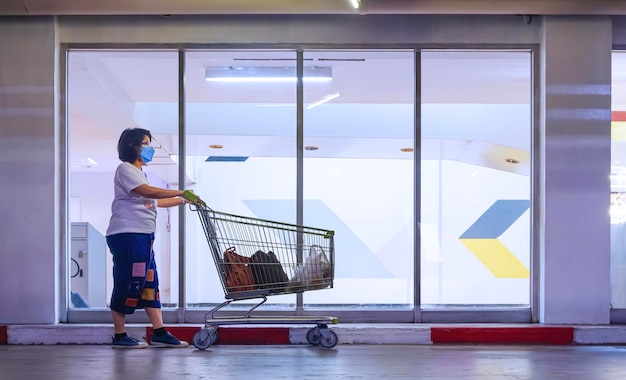 Photo client féminin poussant le caddie devant le mur en verre du supermarché au centre commercial
