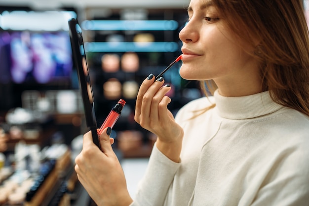 Client féminin testant le crayon à lèvres dans la boutique de maquillage. Choix de cosmétiques en magasin de beauté, maquillage