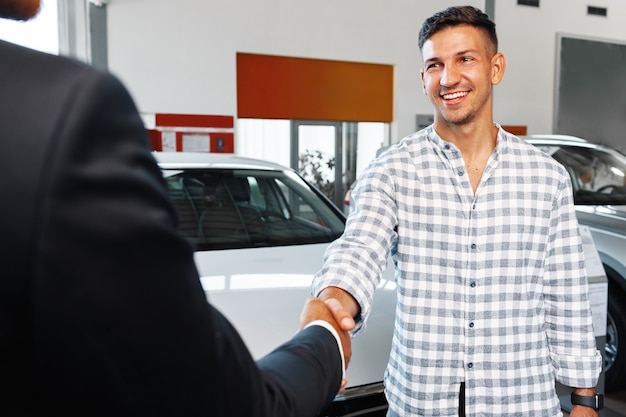 Un client joyeux jeune homme achète une nouvelle voiture chez un concessionnaire