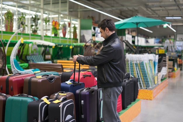 Client masculin choisissant la valise de voyage dans le supermarché