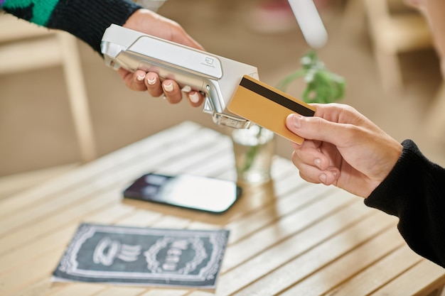 Photo client masculin tenant une carte de crédit près d'un lecteur de cartes coupé la main sur un homme payant dans un café végétalien