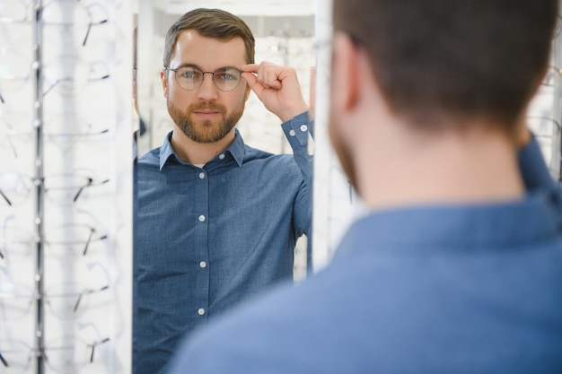 Client satisfait Vue d'un jeune homme heureux portant de nouvelles lunettes debout près d'un rack et d'une vitrine avec des lunettes Homme souriant essayant des lunettes