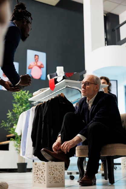 Client senior essayant des chaussures élégantes dans un centre commercial, achetant des vêtements et des accessoires à la mode pour des vêtements décontractés. Homme élégant âgé regardant une nouvelle collection de mode dans un magasin de vêtements