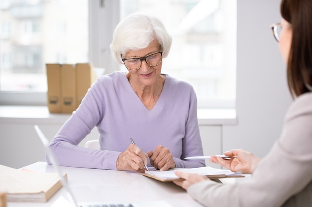 Client senior mettant sa signature dans le contrat d'assurance après discussion de ses termes et conditions avec l'agent lors de la réunion