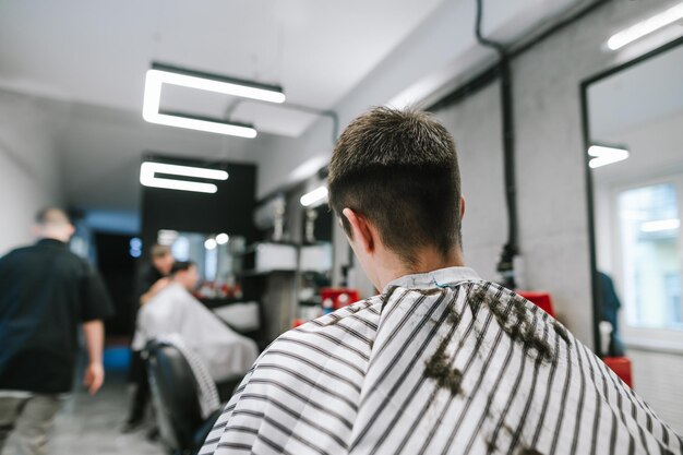 Une cliente brune est également assise dans un peignoir sur une chaise et attend une coupe de cheveux d'un coiffeur