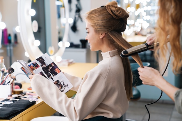 cliente concentrée de belle jeune femme lisant un magazine avec un coiffeur dans un salon.