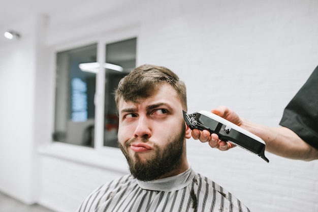 La cliente se coupe les cheveux dans un salon de coiffure et fait une drôle de tête Le coiffeur utilise une tondeuse