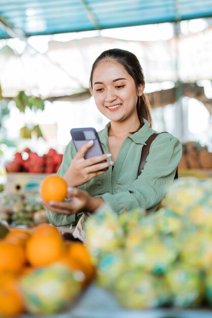 Photo une cliente souriante en prenant une photo du fruit mandarin à l'aide du téléphone