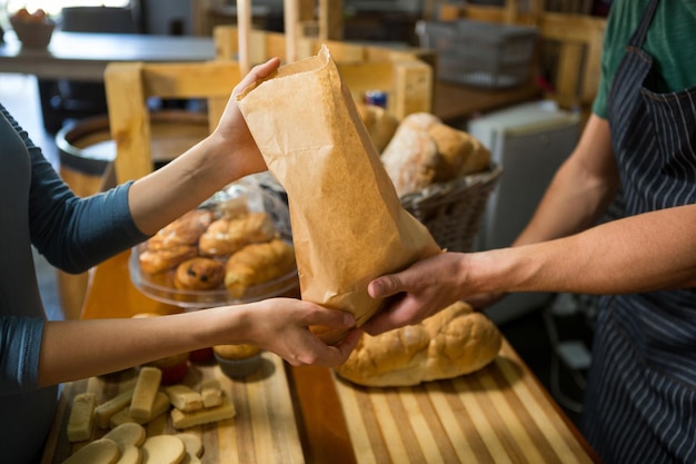 Une cliente souriante reçoit un colis du personnel de la boulangerie au comptoir.