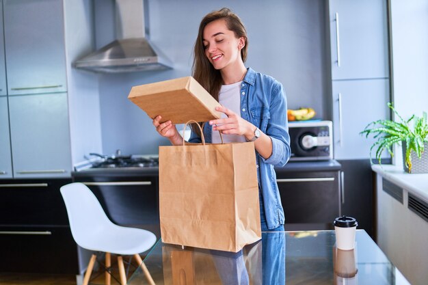 Une cliente souriante, satisfaite, heureuse, décontractée, joyeuse, jeune fille du millénaire a reçu des sacs en carton avec des plats à emporter et des boissons à la maison. Concept de service de livraison rapide