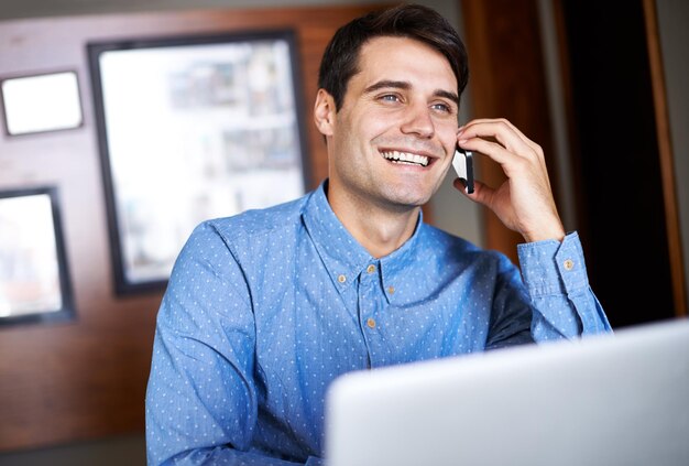 Clients heureux et sourires tout autour Photo d'un jeune homme d'affaires parlant au téléphone assis devant son ordinateur portable