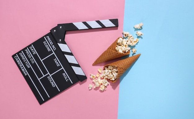 Clin de film, cornets de gaufres à la crème glacée avec pop-corn sur fond pastel lumineux rose et bleu avec ombre profonde, vue de dessus. Le temps du film. Composition à plat