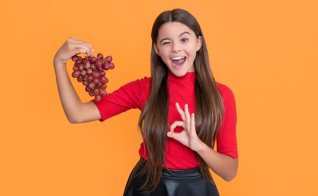 Photo un clin d'œil adolescent tient une grappe de raisin sur fond jaune