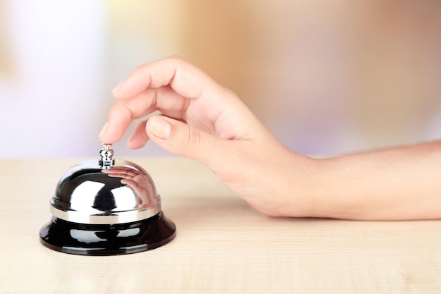 Cloche à main féminine à la réception de l'hôtel sur fond clair