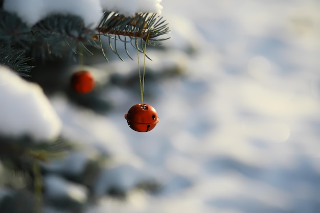 La cloche de Noël rouge est accrochée à une branche enneigée d'un arbre de Noël sur un fond festif de neige blanche Bannière de salutation et de carte de vacances du Nouvel An