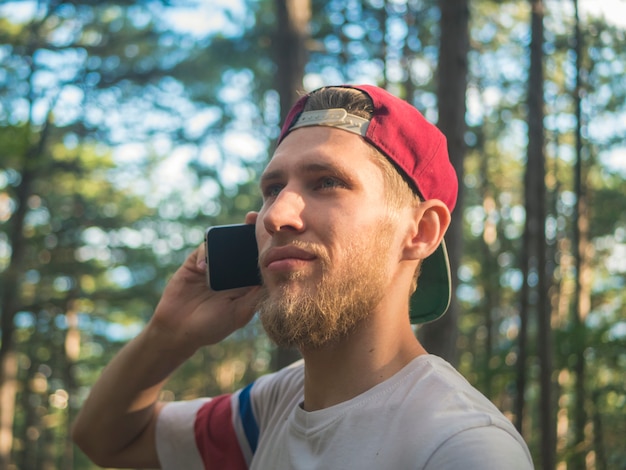 Close portrait de jeune hipster barbu en bonnet parlant via téléphone marchant dans la nature frest en europe suisse