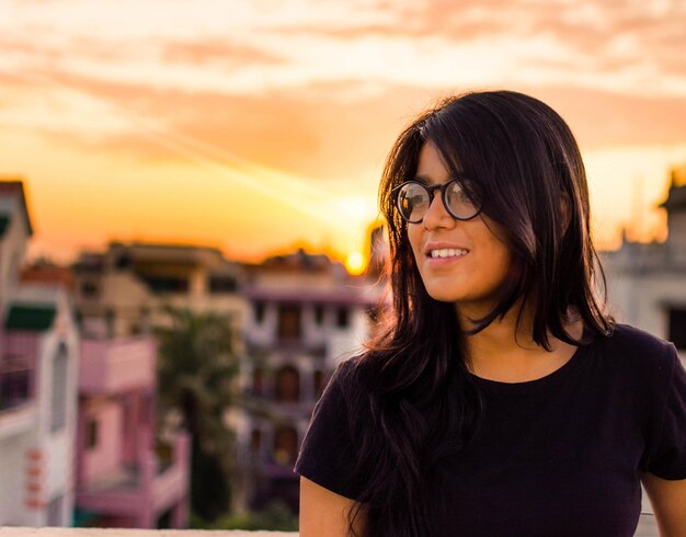 Photo close-up d'une adolescente souriante debout contre un ciel nuageux au coucher du soleil