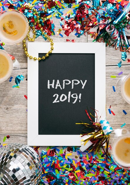 Photo close-up d'une ardoise avec un message de joyeux 2019 au milieu de confettis et de boissons sur la table