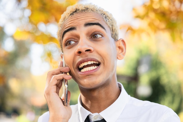 Close-up d'un beau garçon noir aux cheveux blonds avec une expression attentive en train de parler au téléphone portable
