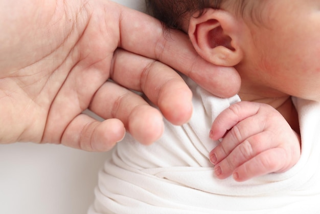 Close-up des bébés petite main tête oreille et paume de la mère Macro photo du nouveau-né après la naissance tenant fermement le doigt des parents sur fond blanc Concept de famille et de maison Soins de santé pédiatrie