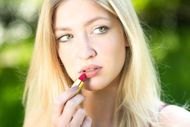 Close-up d'une belle jeune femme appliquant du rouge à lèvres alors qu'elle se tient à l'extérieur