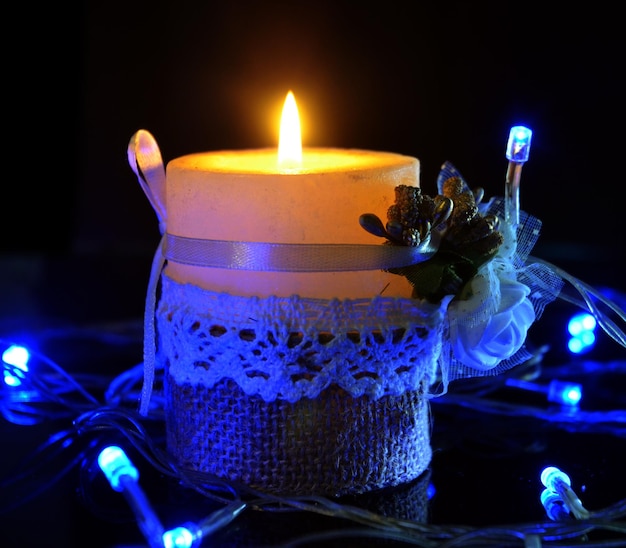 Photo close-up d'une bougie allumée avec des lumières de chaîne éclairées sur une table sur un fond noir