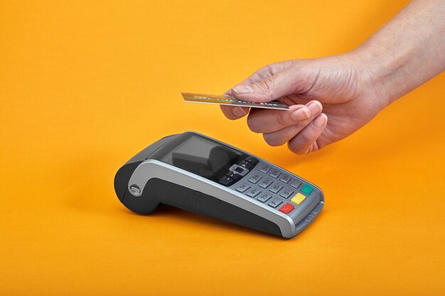 Close-up des boutons de la machine de paiement avec une main humaine tenant une carte en plastique à proximité sur un fond jaune