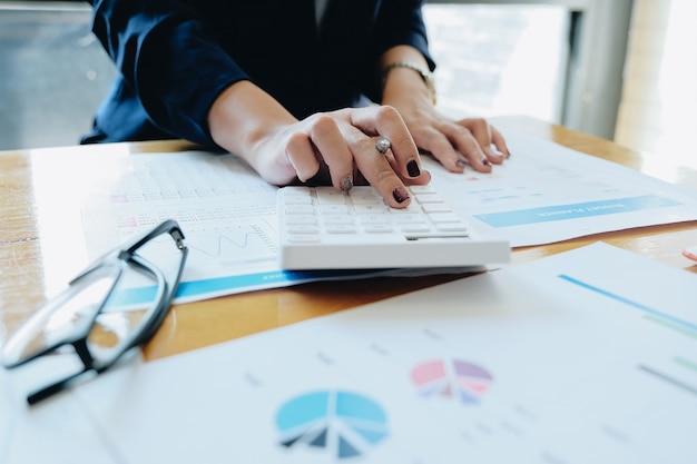 Close Up Businesswoman Using Calculator And Laptop For Do Math Finance On Desk In Wooden Desk In Office And Business Working Background, Tax, Accounting, Statistics And Analytic Research Concept