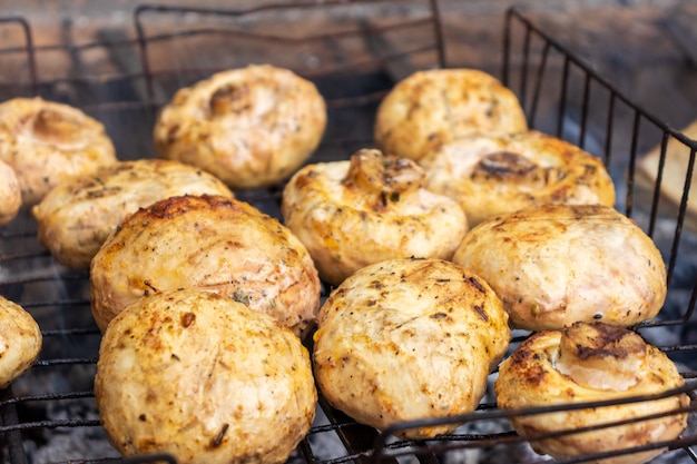 Close-up de champignons sur le gril du barbecue avec la main du cuisinier