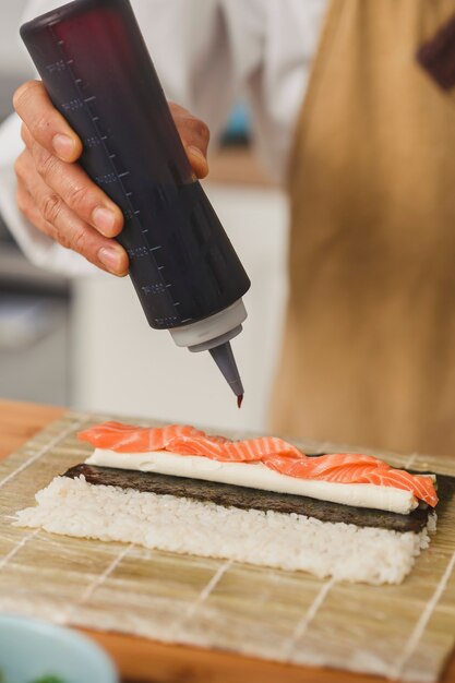 Close up chef faisant le processus de rouleau de sushi sushi ajoute de la sauce aux sushis