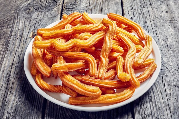 Close-up de churros - dessert traditionnel espagnol et mexicain sur un plateau blanc sur une vieille table en bois rustique gris, vue d'en haut