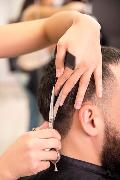 Close-up coiffeuse coupe les cheveux du client de l'homme.