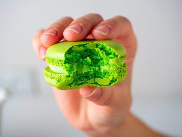 Close-up d'un cookie macaron vert grignoté dans votre main sur un fond blanc