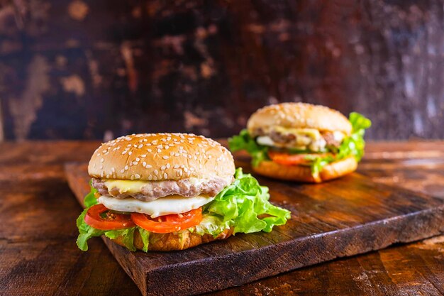 Close-up d'un délicieux hamburger frais fait maison avec salade, fromage, oignon et tomate sur une planche en bois rustique sur une table en bois