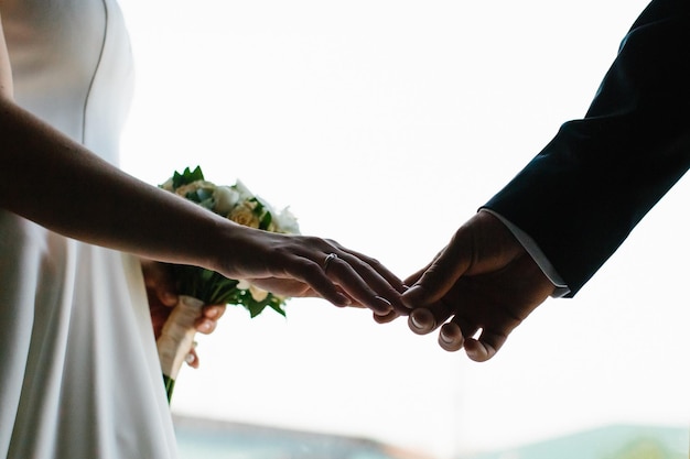 Photo close-up du couple de mariés se tenant par la main contre le ciel