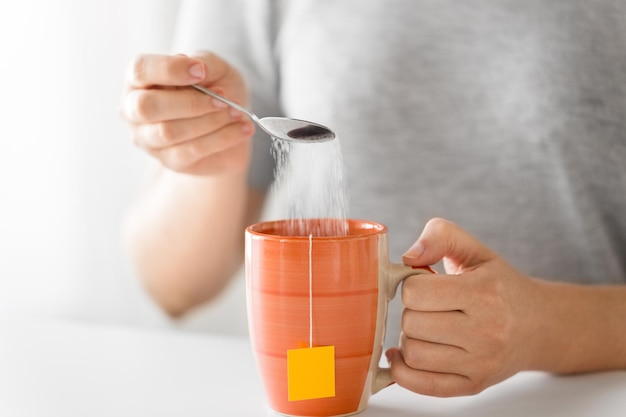 Close-up d'une femme ajoutant du sucre à une tasse de thé