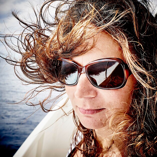 Close-up d'une femme aux cheveux ébouriffés portant des lunettes de soleil dans un bateau