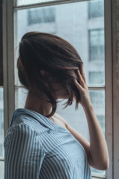 Close-up d'une femme couvrant le visage avec des cheveux contre la fenêtre